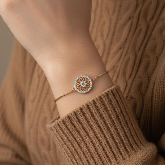 Abidii Everly Bracelet – slim gold-tone bracelet with a round center motif and pavé halo, displayed on dark fabric, showing its radiant, detailed design.