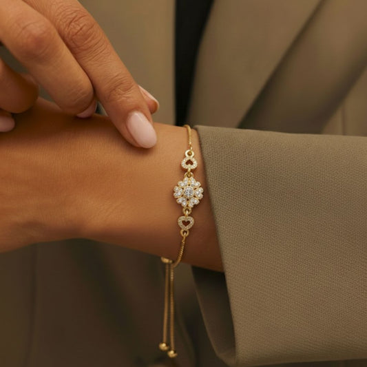 Abidii Affection Bracelet – slim gold-tone bracelet with a central flower motif and pavé hearts on each side, displayed on dark fabric, showing its delicate, romantic design.