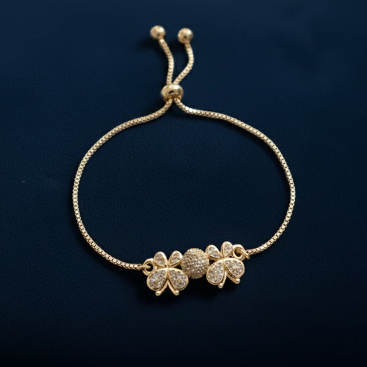 Abidii Angel Bracelet – slim gold-tone bracelet with two clover-like motifs and a pavé center bead, displayed on dark fabric, showing its delicate, winged design.