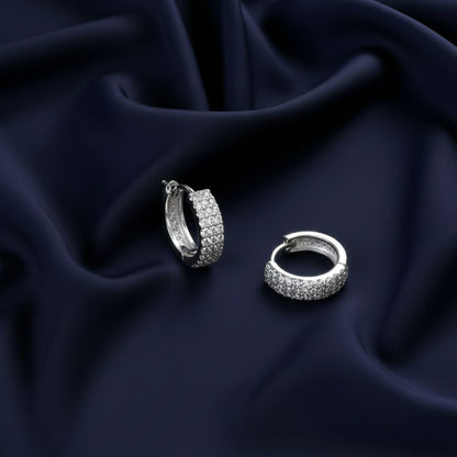 Abidii Luna Hoops – silver tone pavé hoop earrings displayed on a soft fabric surface, highlighting their minimal shape and cool shine.