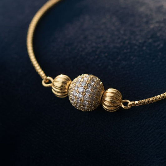 Abidii Orbit Bracelet – slim gold-tone bracelet with a central pavé bead and two smooth accent beads, displayed on dark fabric, showing its minimal, luminous design.