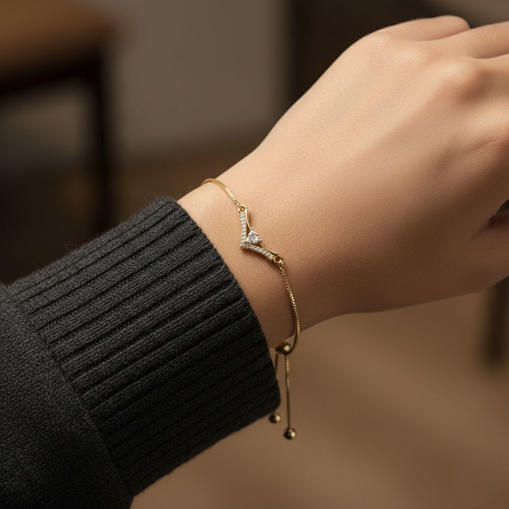 Abidii Tiara Bracelet – slim gold-tone bracelet with a V-shaped pavé centre and three stones in a triangle, displayed on dark fabric, showing its delicate crown-like design.